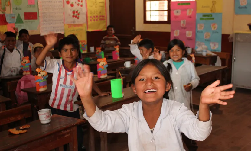 Smiling school children waving and enjoying their time in a colorful classroom.